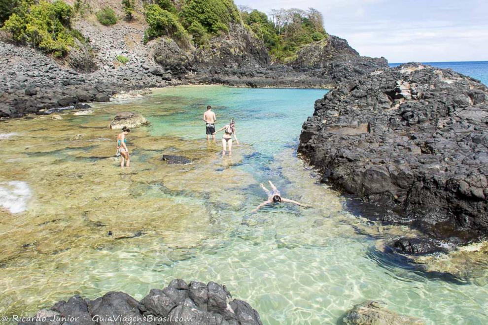 Imagem de turistas nadando nas águas transparentes da Baía dos Porcos em Fernando de Noronha.